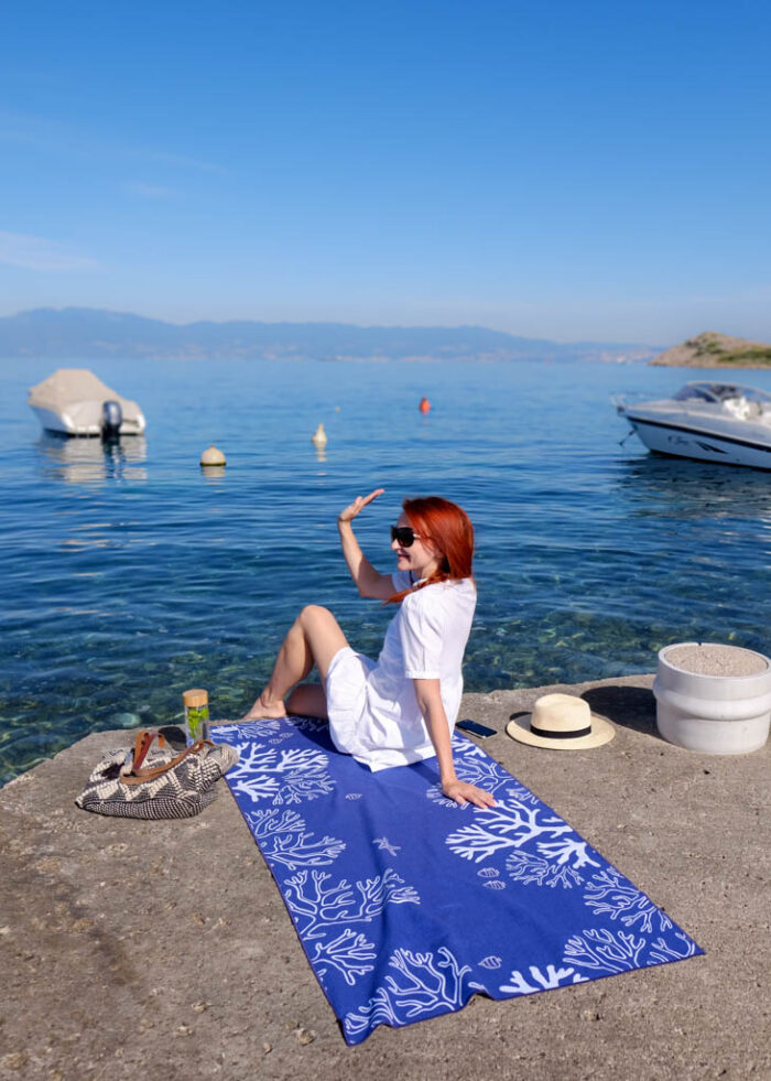 Žena sedí u moře na tmavé elegantní plážové osušce Coral Reef