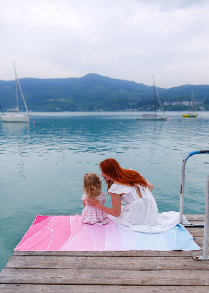 Žena a dcera na molu u jezera sedí na osušce k bazénu a na cesty Life is a Beach Pink