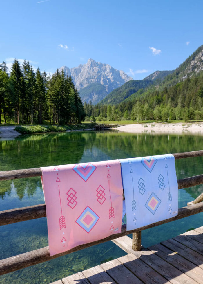 Přes zábradlí pověšené dvě funkční plážové osušky NAYAVITA v designu Tribal v modré a růžové