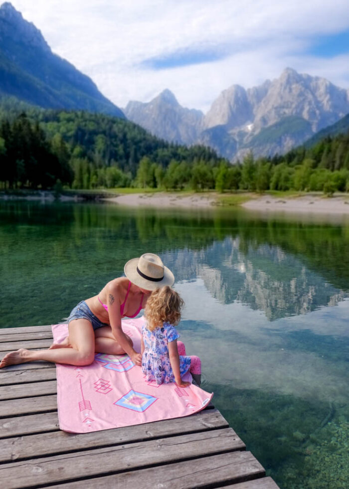 Matka s dcerou u jezera na molu sedí na růžové lehké osušce do kufru Tribal od NAYAVITA